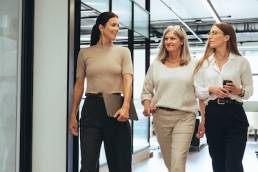 Three cheerful businesswomen walking together in an office, female leaders
