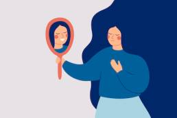 Young woman looks at the mirror and sees her happy reflection. Self-acceptance and confidence concept.
