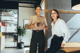 Cheerful female entrepreneurs smiling at the camera while standing in a modern co-working space