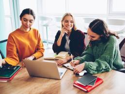 Successful young female entrepreneurs creating new working schedule and collaborating on developing design company during briefing sitting at meeting table with modern laptop device in stylish office