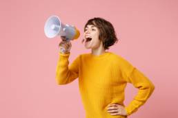 woman in a yellow jumper using a megaphone to get her voice heard