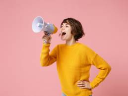 woman in a yellow jumper using a megaphone to get her voice heard