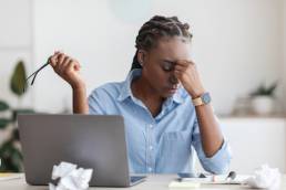 Deadline Stress. Overworked Black Female Entrepreneur Massaging Nosebridge At Workplace In Office, Exhausted After Using Laptop