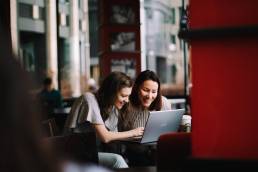 Flexible working, two female colleagues working together in cafe, hybrid working