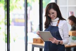 Young woman in retail, smiling down at tablet, retail apprenticeship