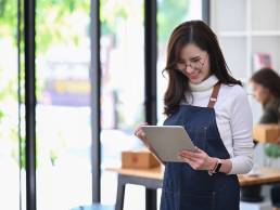 Young woman in retail, smiling down at tablet, retail apprenticeship