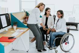 Disabled businesswoman in wheelchair and her female coworkers planning while working at corporate office.