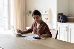 Woman sat at table busy in personal expenses management, use calculator calculate household utilities, pay bills through secure e-banking app on laptop. Finances, accounting concept