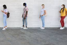 people standing in a queue and waiting - Young people with social distancing and wearing protective face masks - Concept of the new normality and social distancing