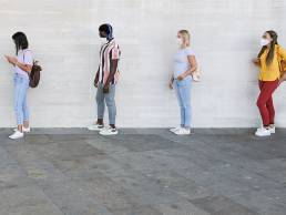 people standing in a queue and waiting - Young people with social distancing and wearing protective face masks - Concept of the new normality and social distancing