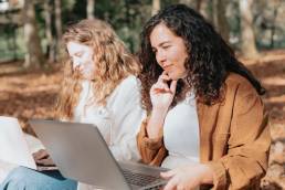 Two happy smiling women working outside on bench, working overseas