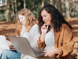 Two happy smiling women working outside on bench, working overseas