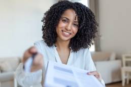 Smiling woman signing form, handing over pen and paper to colleague
