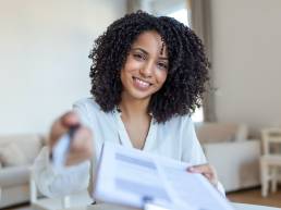 Smiling woman signing form, handing over pen and paper to colleague