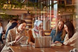 Diversity Female Working At Bistro. Women Meeting In Cafe. Group Of Four Smiling Girls Sitting In Restaurant And Discussing. Freelance As Lifestyle.