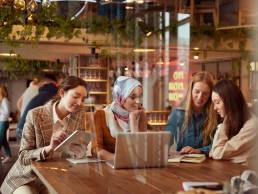 Diversity Female Working At Bistro. Women Meeting In Cafe. Group Of Four Smiling Girls Sitting In Restaurant And Discussing. Freelance As Lifestyle.