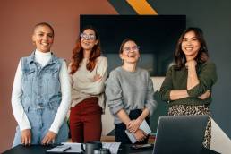 Successful female entrepreneurs smiling cheerfully while standing behind a table in a boardroom. Group of multicultural businesswomen working together in a modern office.
