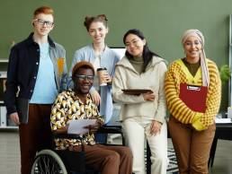 Portrait of diverse creative team looking at camera with cheerful smiles while posing in office, wheelchair user inclusion