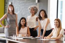 Five female colleagues at a work meeting smiling to camera