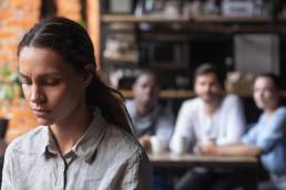 Upset mixed race woman suffering from bullying, discrimination, excluded girl having problem with bad friends, feeling offended and hurt, sitting alone in cafe, avoiding people, social outcast